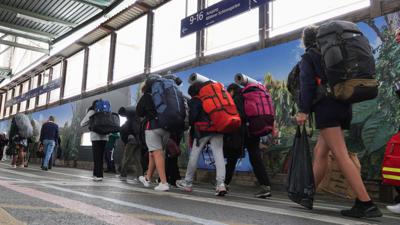 Fahrgäste mit Rucksäcken gehen am ersten Ferientag in Baden-Württemberg auf dem Hauptbahnhof in Stuttgart zu einem Zug.