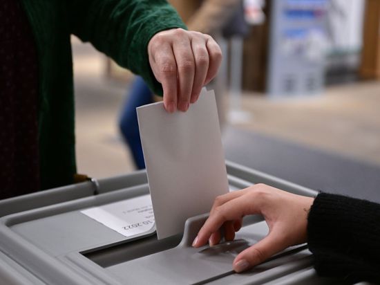 Ein Wähler steckt bei einer Wahl seinen Wahlzettel in eine Urne.