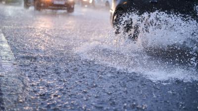 Autos fahren bei starkem Regen durch tiefe Pfützen.