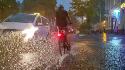 Ein Fahrradfahrer und ein Auto fahren über eine vom Regen überschwemmte Straße.