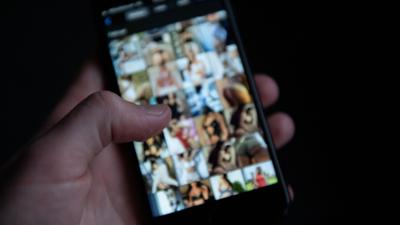 Ein Mann schaut sich auf einem Smartphone pornografische Bilder an.