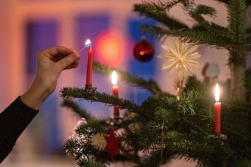 Eine Frau zündet eine Kerze an einem Weihnachtsbaum an.
