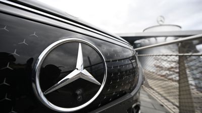 Das Logo der Automarke Mercedes-Benz ist an der Front eines Mercedes-Benz Fahrzeugs angebracht. Das Auto steht vor einer Mercedes-Benz Niederlassung.