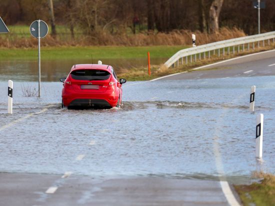 Ein Auto fährt auf einer mit Hochwasser überfluteten Straße zwischen Daugendorf und Unlingen.