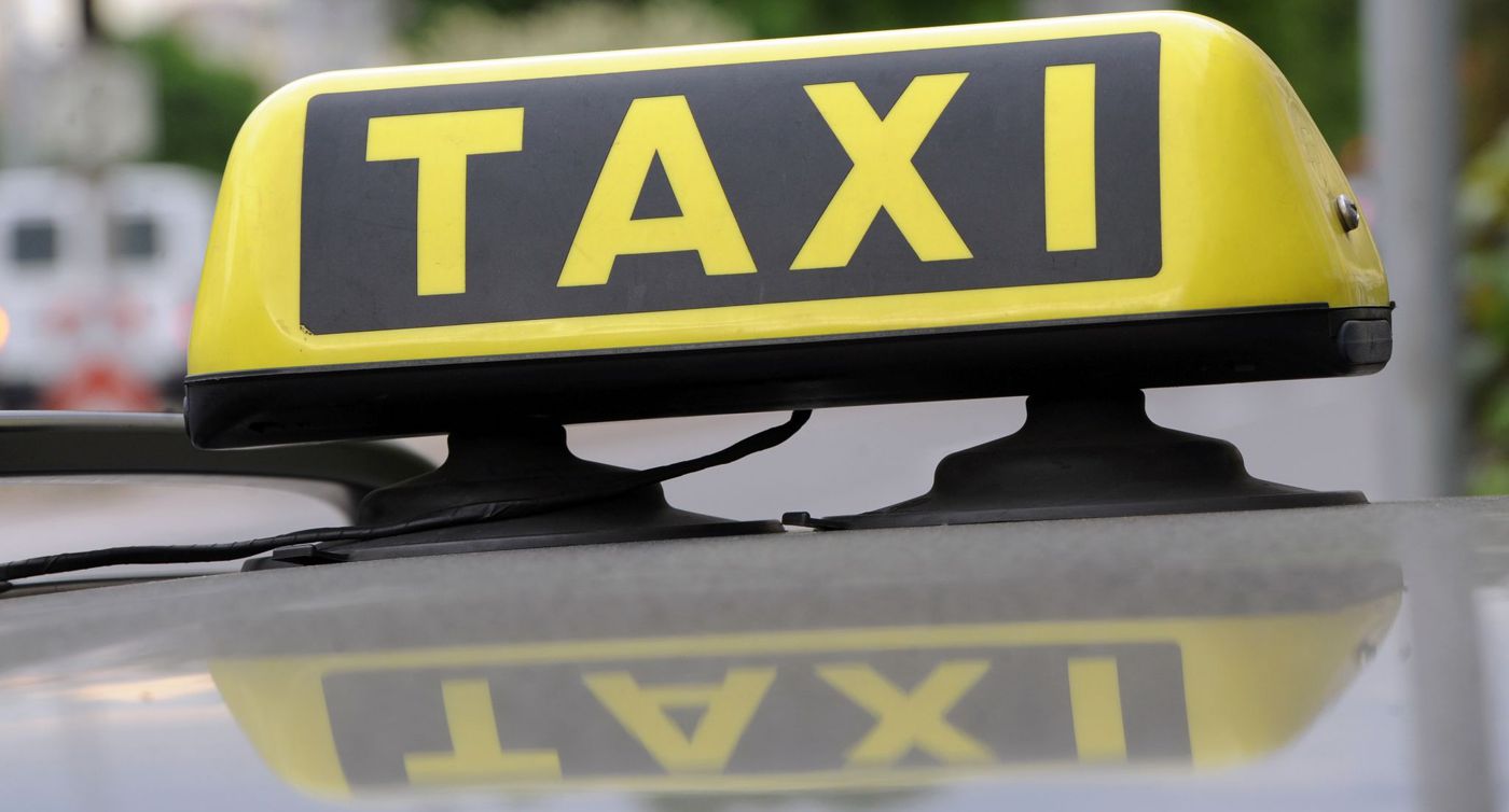Ein Taxischild spiegelt sich in einem Autodach.