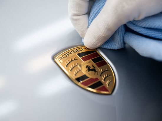 Ein Mitarbeiter der Porsche AG reinigt im Stammwerk in Zuffenhausen das Porsche-Wappen auf einer Motorhaube.