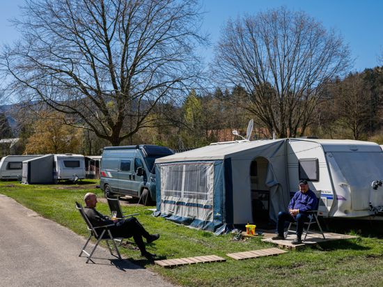 PRODUKTION – 04.04.2023, Baden-Württemberg, Kirchzarten: Zwei Männer sitzen in der Sonne vor einem Wohnwagen auf einem Campingplatz. Die Saison auf vielen Campingplätzen im Südwesten startet mit den Osterfeiertagen. (zu dpa-Korr: „Im Zelt oder auf Achse – Camping boomt im Südwesten“) Foto: Philipp von Ditfurth/dpa +++ dpa-Bildfunk +++