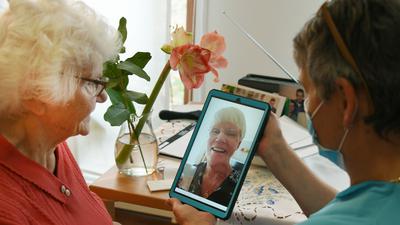 Im Haus der Generationen der Paul-Riebeck-Stiftung in Halle/Saale hält die Pflegeassistentin Inge Schenk ein Tablett für die 91-jährige Heimbewohnerin Hildegard Zipfel in der Hand, deren Tochter per Videotelefonie zugeschaltet ist.