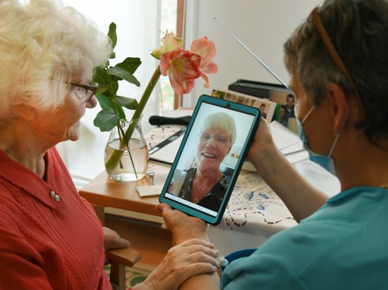 Im Haus der Generationen der Paul-Riebeck-Stiftung in Halle/Saale hält die Pflegeassistentin Inge Schenk ein Tablett für die 91-jährige Heimbewohnerin Hildegard Zipfel in der Hand, deren Tochter per Videotelefonie zugeschaltet ist.