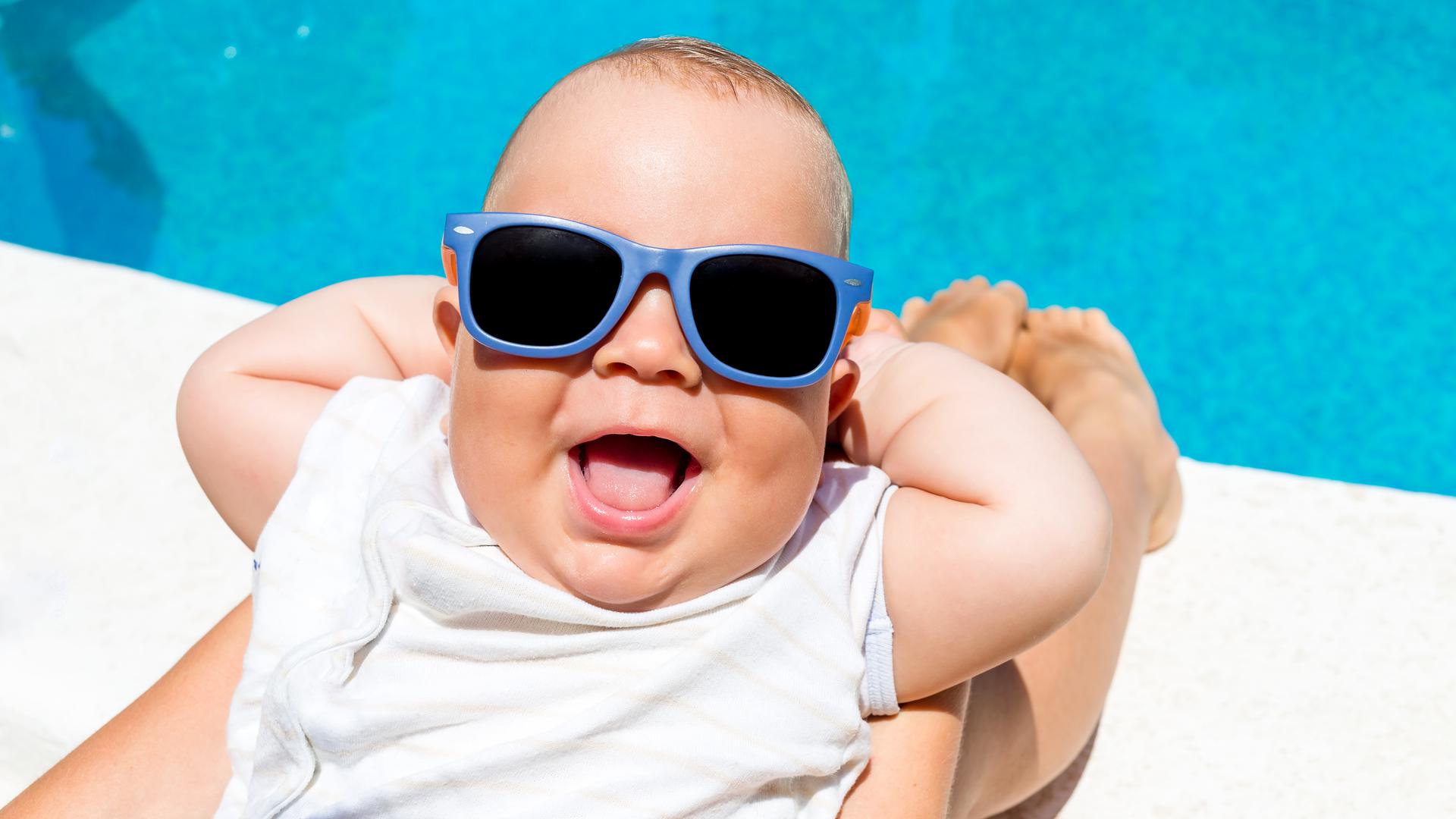 Ein fröhliches Baby mit einer Sonnenbrille entspannt am Pool.