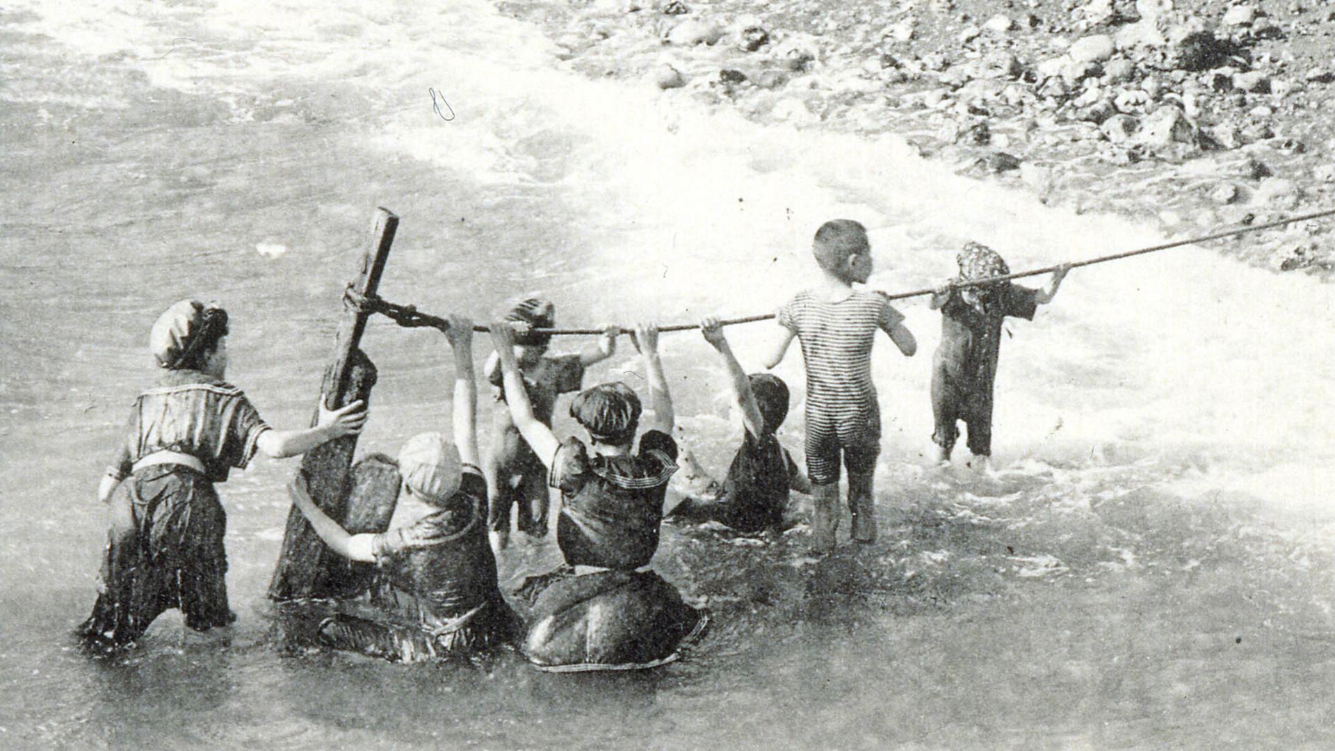 Das Postkartenmotiv vom Anfang des 20. Jahrhunderts zeigt Nichtschwimmer, die sich beim Baden in einem natürlichen Gewässer an einem Seil festhalten.