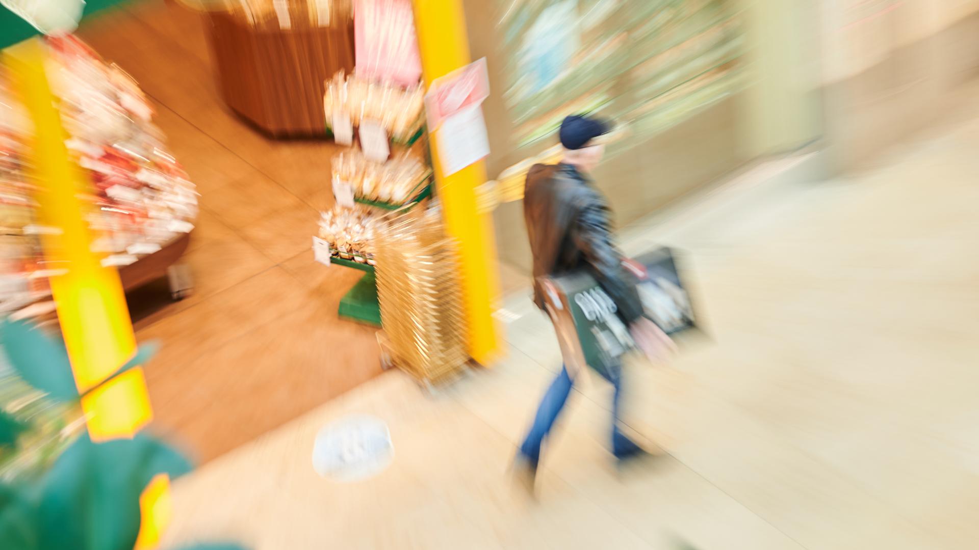 In den Schönhauser Allee Arcaden trägt ein Mann einen Karton, während an Geschäften vorbeigeht (Zoom-Effekt durch Bewegung des Objektives). 