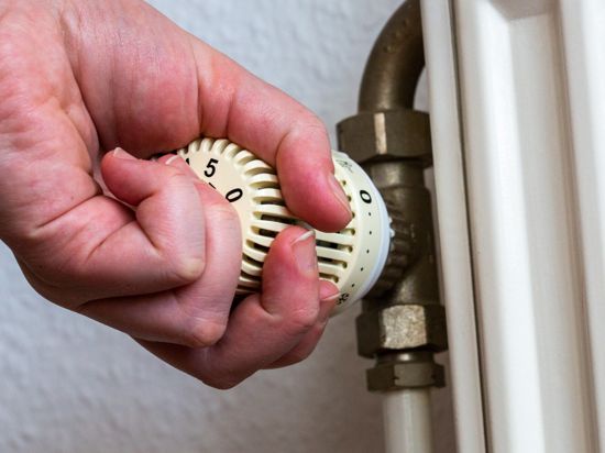 Eine Person dreht am Thermostat einer Heizung in einer Wohnung.