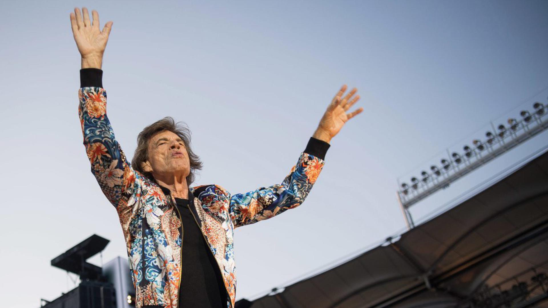 Mich Jagger mit Händen in der Luft von unten in einem Stadion.