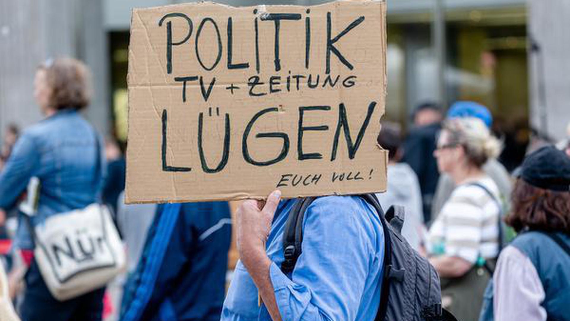Ein Mann hält ein Plakat mit der Aufschrift « Politik, TV und Zeitung lügen euch voll!».