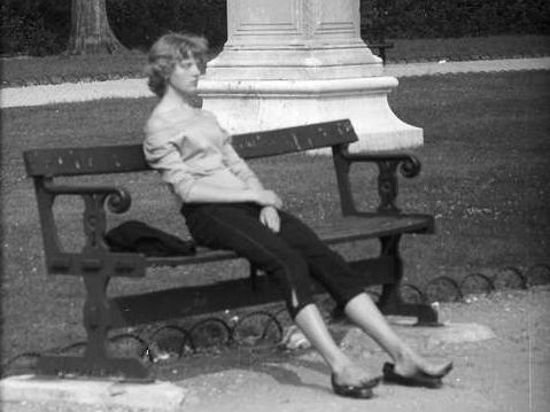 Eine junge Frau in Caprihosen sitzt auf einer Parkbank.