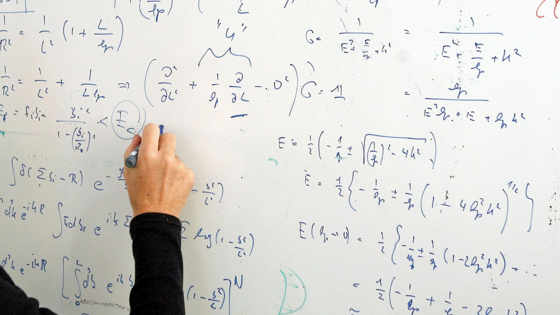 Ein Wissenschaftler steht an einer Tafel die mit Formeln beschrieben ist.