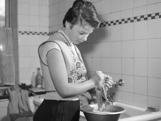 Eine junge Frau wäscht in den 1950er Jahren Textilien mit der Hand.