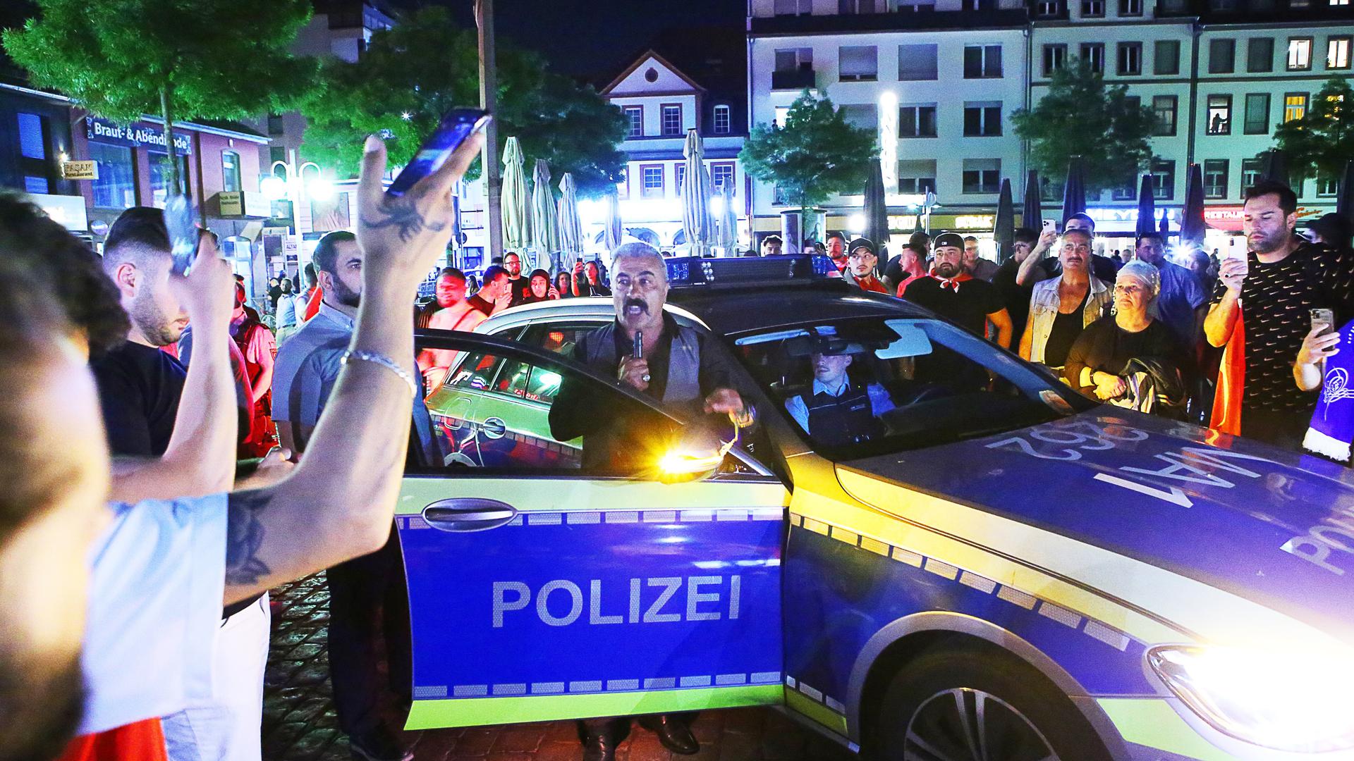 Die Polizei ist in der Innenstadt im Einsatz, während Menschen um ein Polizeiauto stehen. Nach Bekanntgabe des Sieges von Recep Tayyip Erdoğan bei der Präsidentenwahl in der Türkei ist es am Sonntagabend in Mannheim zu Auseinandersetzungen gekommen.