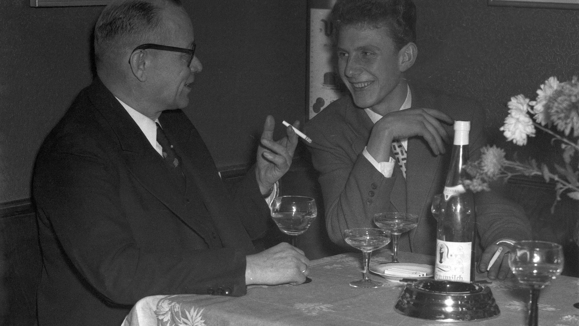 Zwei Männer unterhalten sich bei einer Flasche Wein und anderen alkoholischen Getränken.