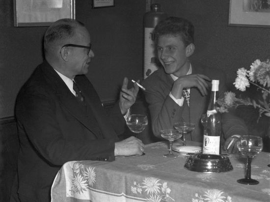 Zwei Männer unterhalten sich bei einer Flasche Wein und anderen alkoholischen Getränken.