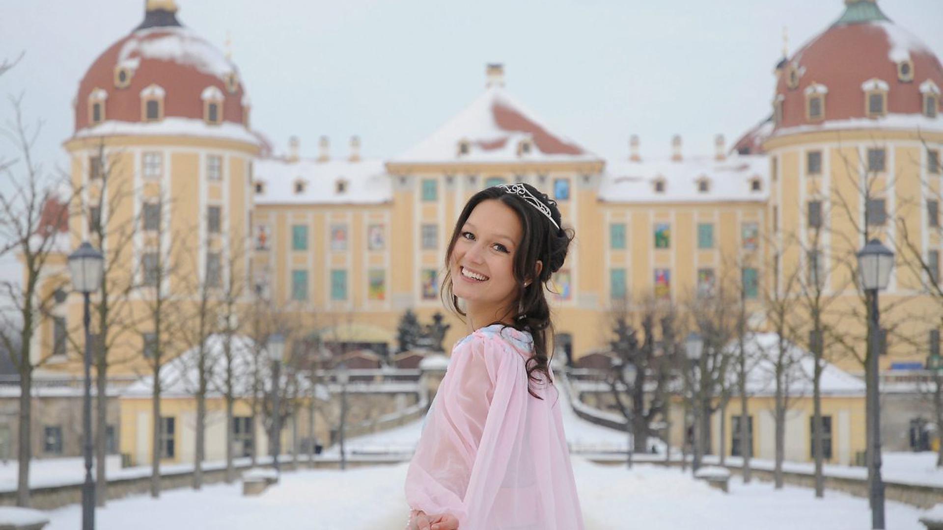 Ein Mädchen in rosa Kleid und Krone vor dem gelben Schloss Moritzburg.