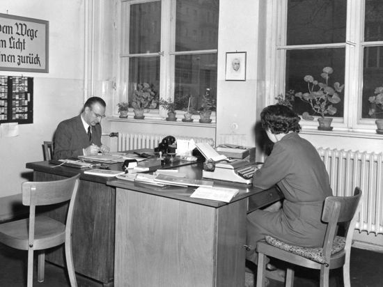 Ein Mann und eine Frau sitzen bei der Arbeit in einem Büro der 1950er Jahre.