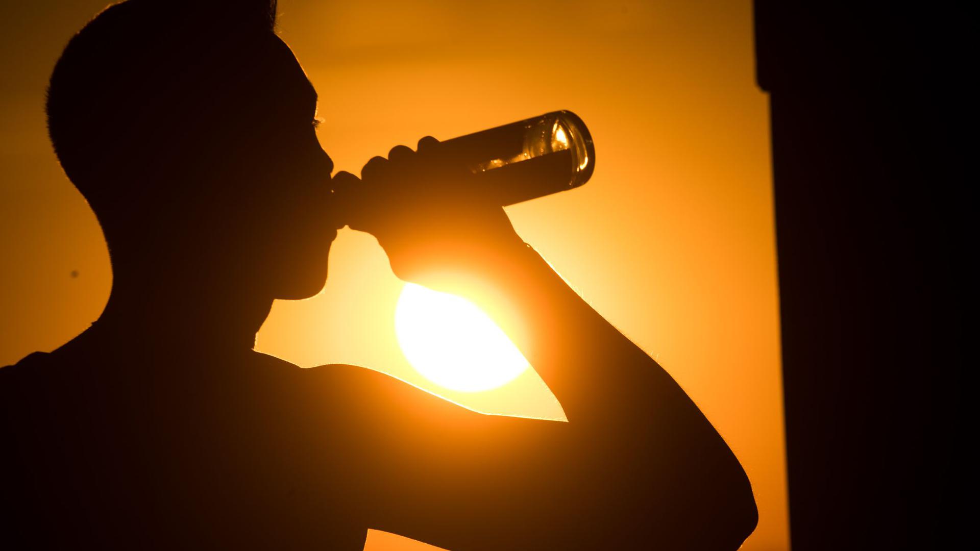 Ein junger Mann sitzt auf dem Kronsberg, und trinkt Bier, während am Horizont die Sonne untergeht.