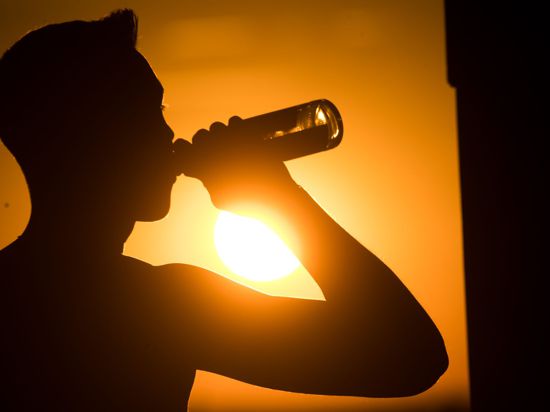 Ein junger Mann sitzt auf dem Kronsberg, und trinkt Bier, während am Horizont die Sonne untergeht.
