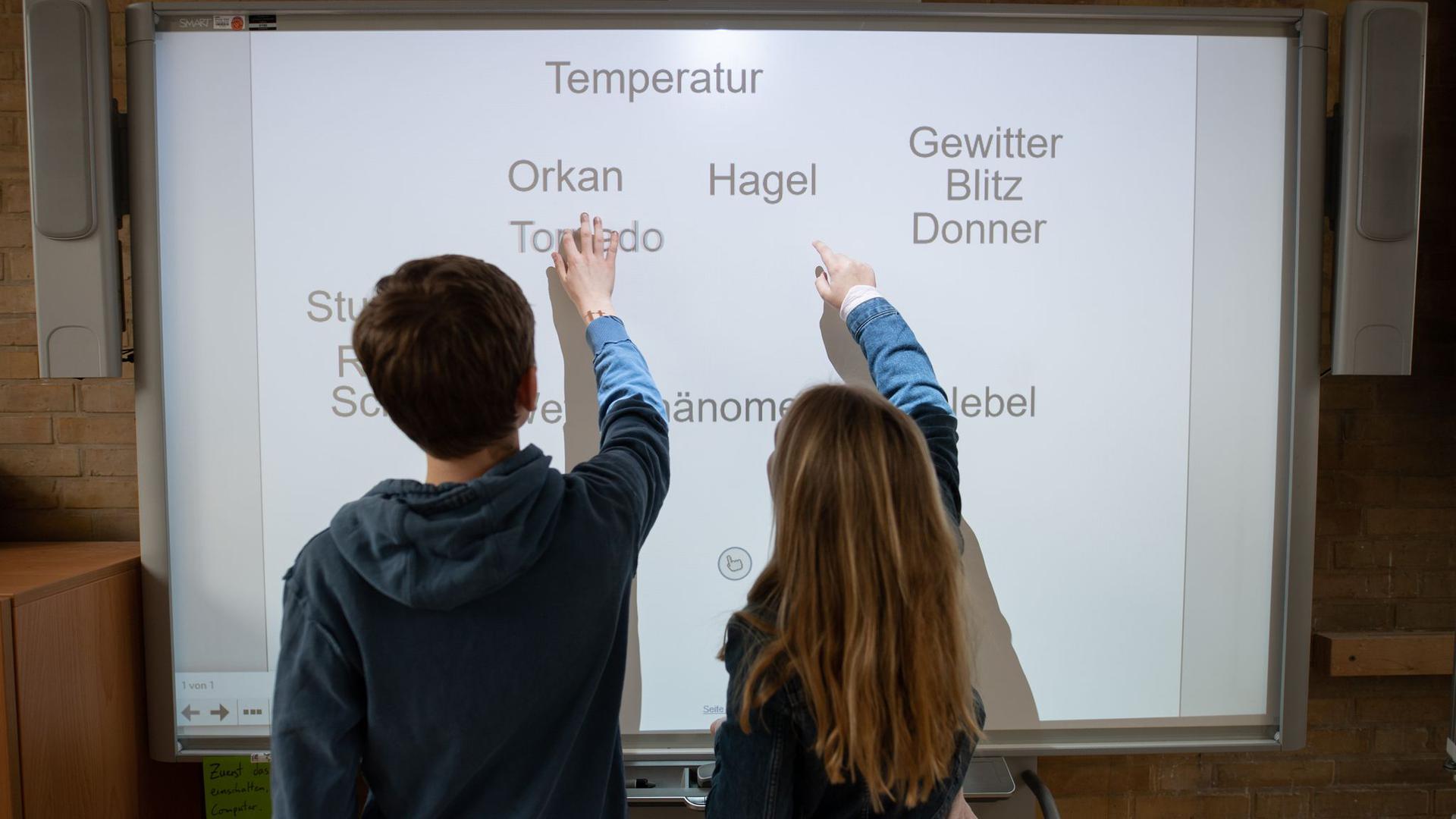 Ein Schüler und eine Schülerin arbeiten an einem Smartboard.