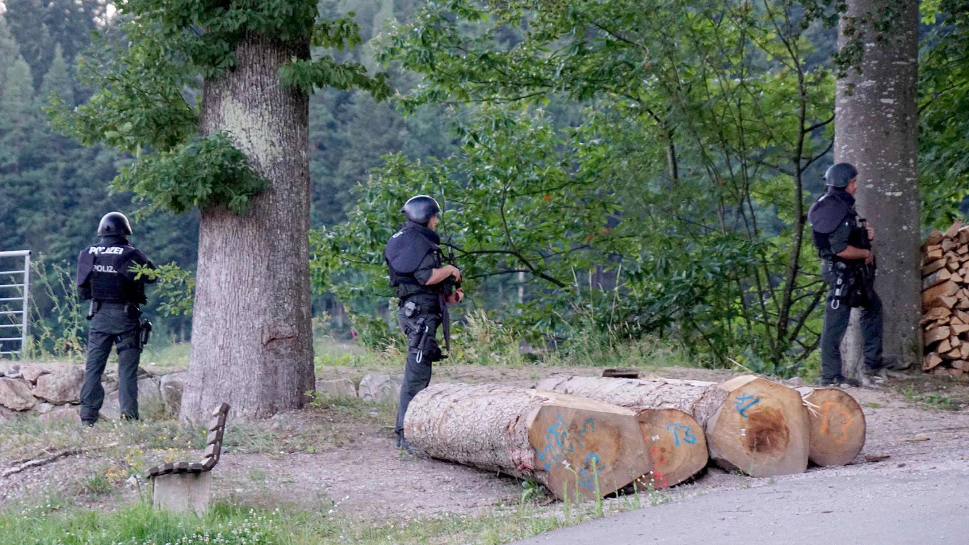 Polizisten stehen vor einem Waldstück an einer Straße bei Oppenau. Am Vortag hatte ein Mann bei einer Kontrolle Polizisten bedroht und entwaffnet.