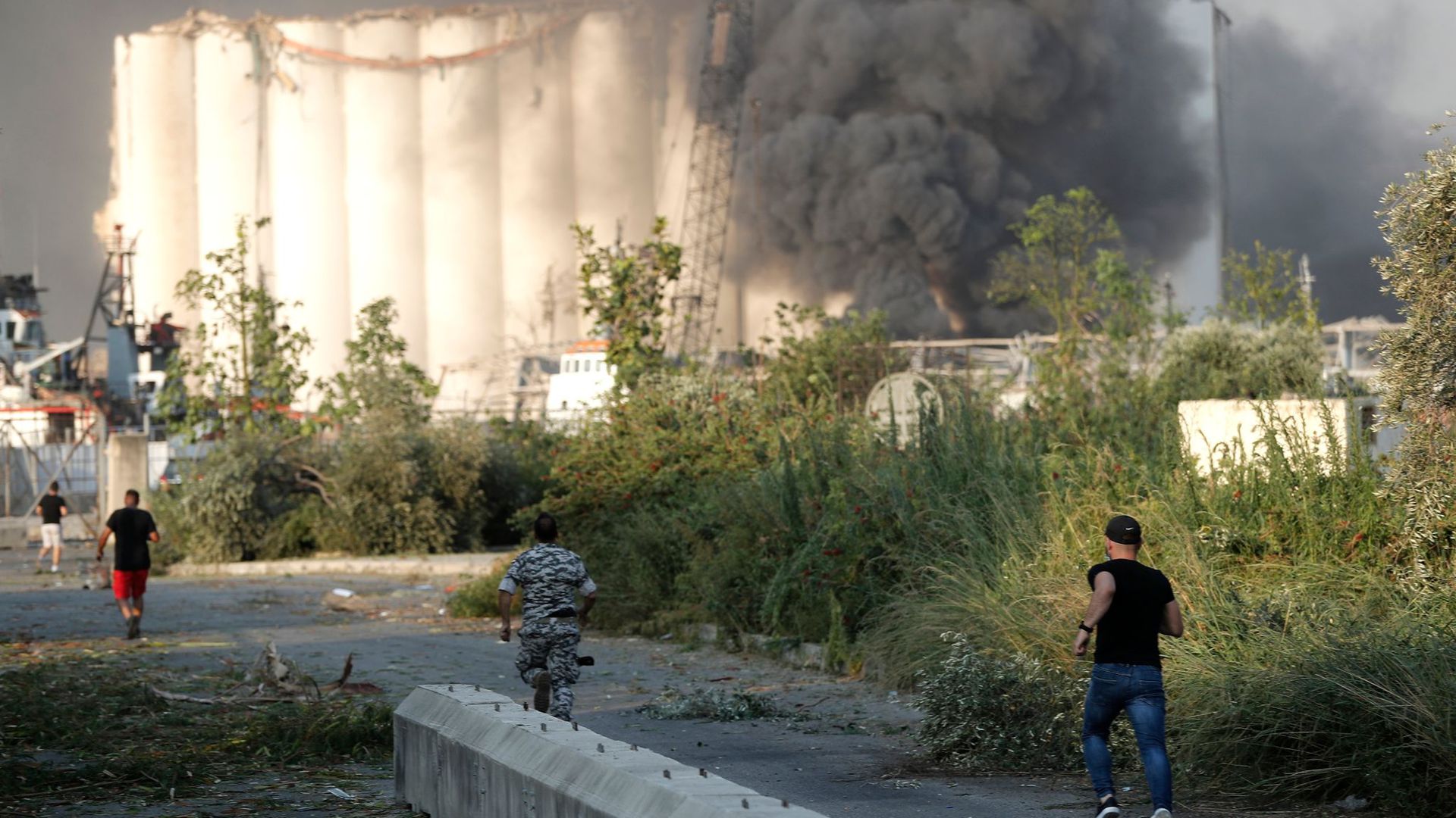 Sicherheitsleute laufen zum Ort der Explosion im Hafen von Beirut, während über dem Gebäude Rauch aufsteigt.