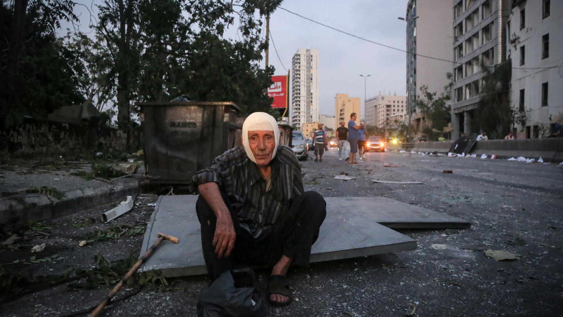 Ein älterer Herr sitzt nach der Explosion im Hafen von Beirut mit einem Verband auf dem Kopf auf der Straße.