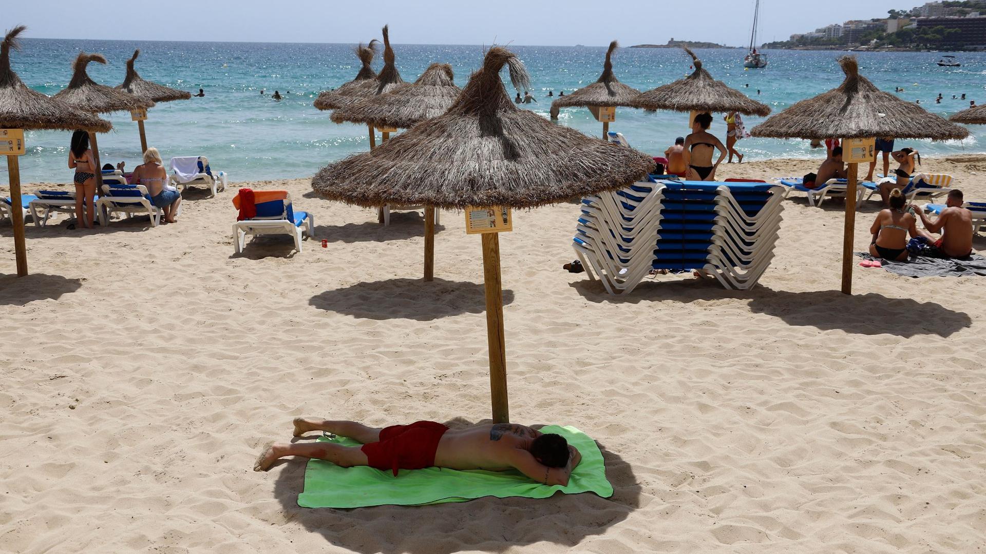 Ein Mann liegt unter einem Sonnenschirm am Strand von Cala Major, Mallorca. Die Bundesregierung warnt vor Reisen auf die Insel.