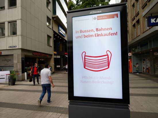 Ein Werbebildschirm weist in der Kölner Innenstadt auf die Maskenpflicht in Geschäften und im Nahverkehr hin.