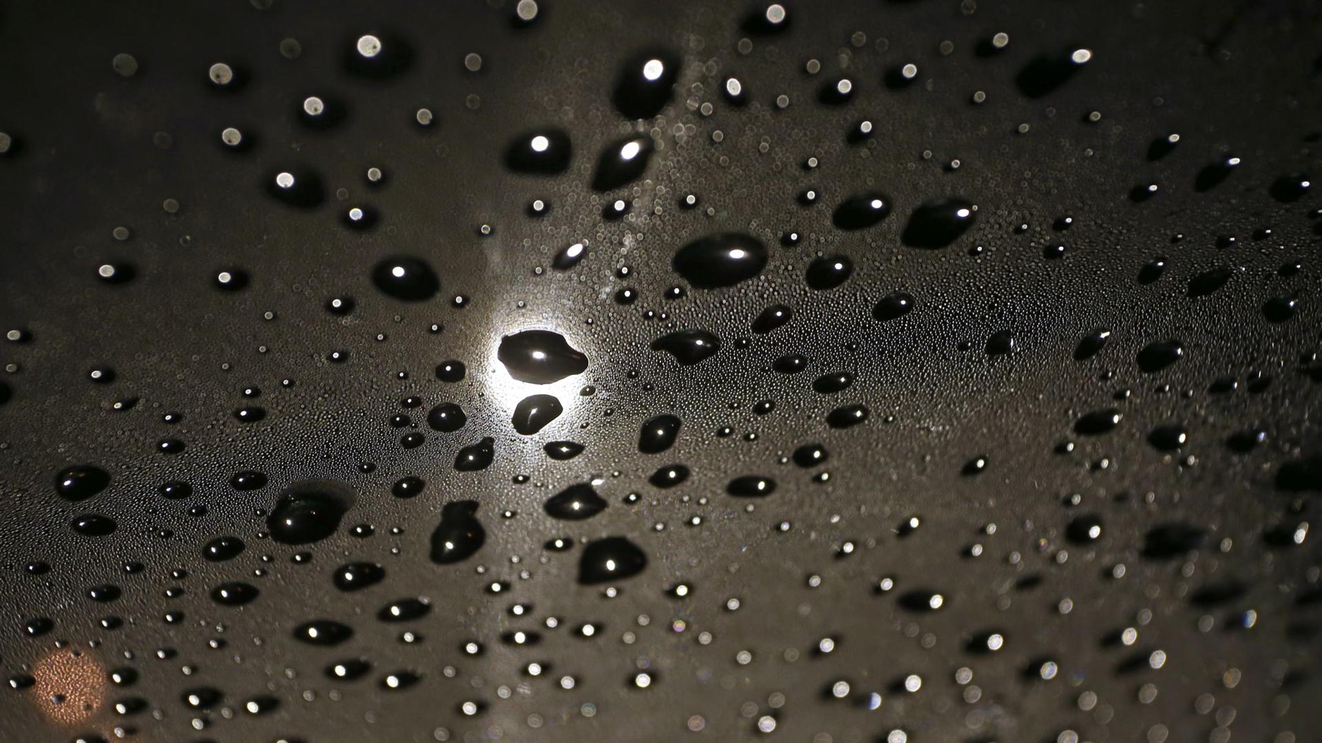 Regentropfen liegen im Licht einer Straßenlaterne auf der Windschutzscheibe eines Autos. Hoch „Manfreed“ zieht weiter, es wird kühler und nass.