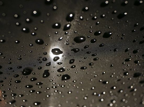Regentropfen liegen im Licht einer Straßenlaterne auf der Windschutzscheibe eines Autos. Hoch „Manfreed“ zieht weiter, es wird kühler und nass.