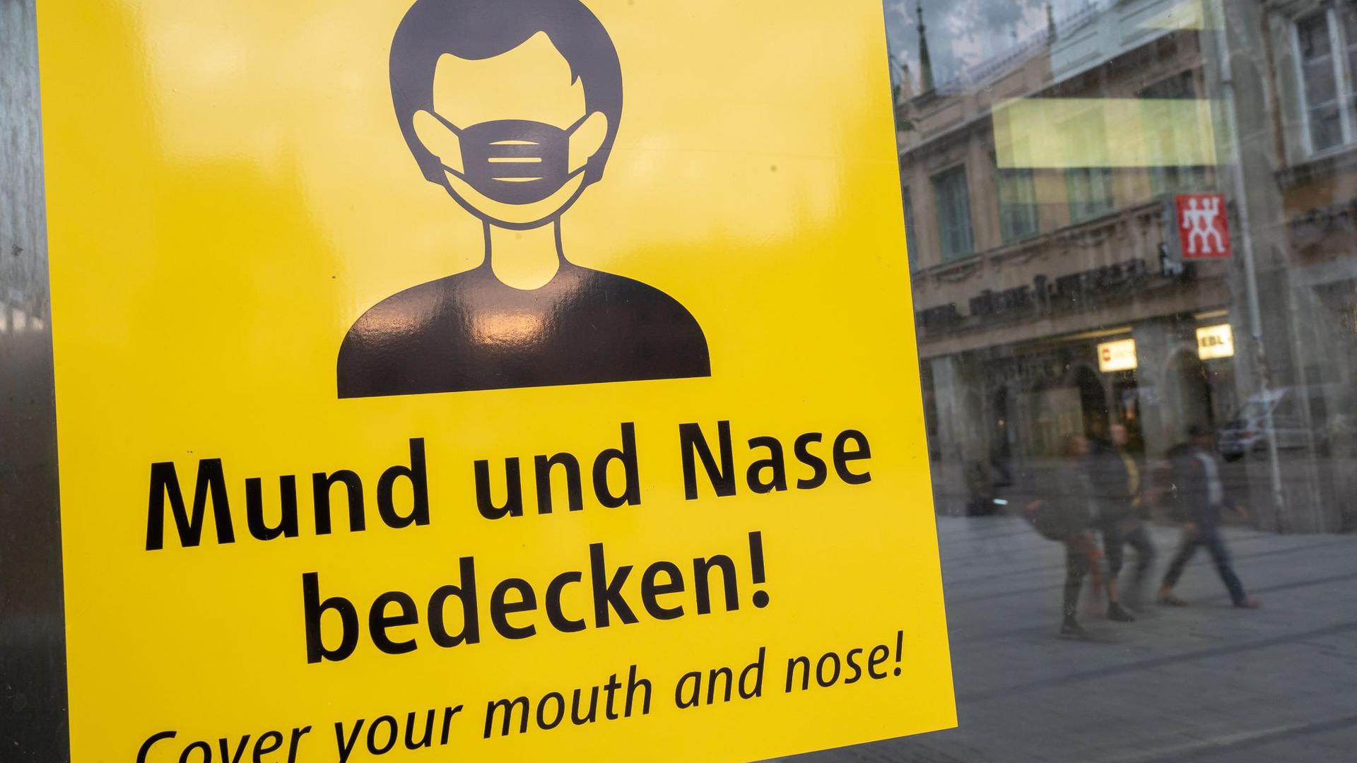 Auf dem Münchener Marienplatz fordert ein Schild zum Tragen eine Mund-Nasen-Bedeckung auf.