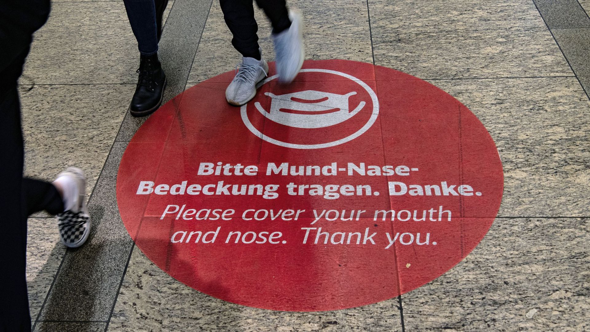 Der Aufkleber „Bitte Mund-Nase-Bedeckung tragen. Danke“ ist im Bahnhof am Alexanderplatz in Berlin auf dem Boden befestigt.