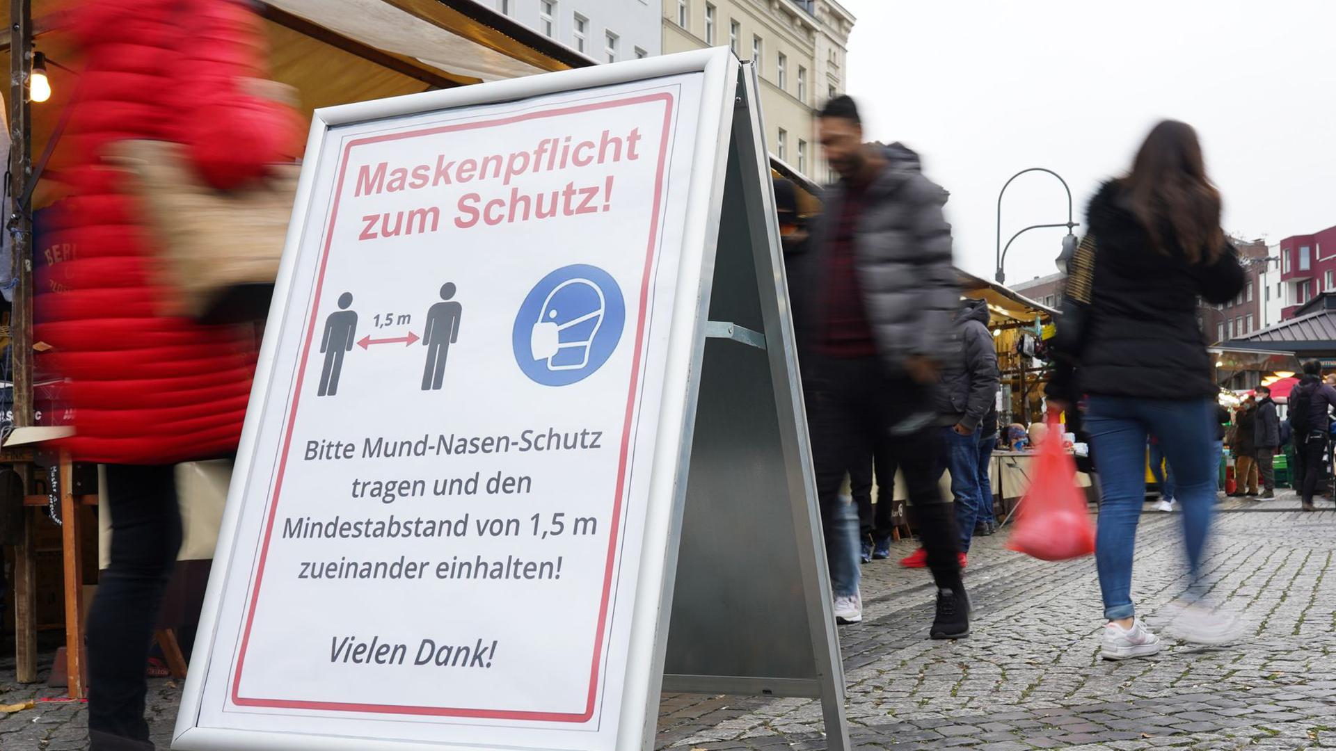 Ein Schild weist auf einem Wochenmarkt in Berlin auf Maskenpflicht und Abstandsgebot hin.