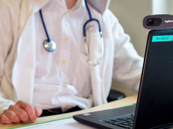Ein Hausarzt sitzt während einer Videosprechstunde in seiner Praxis vor einem Laptop.