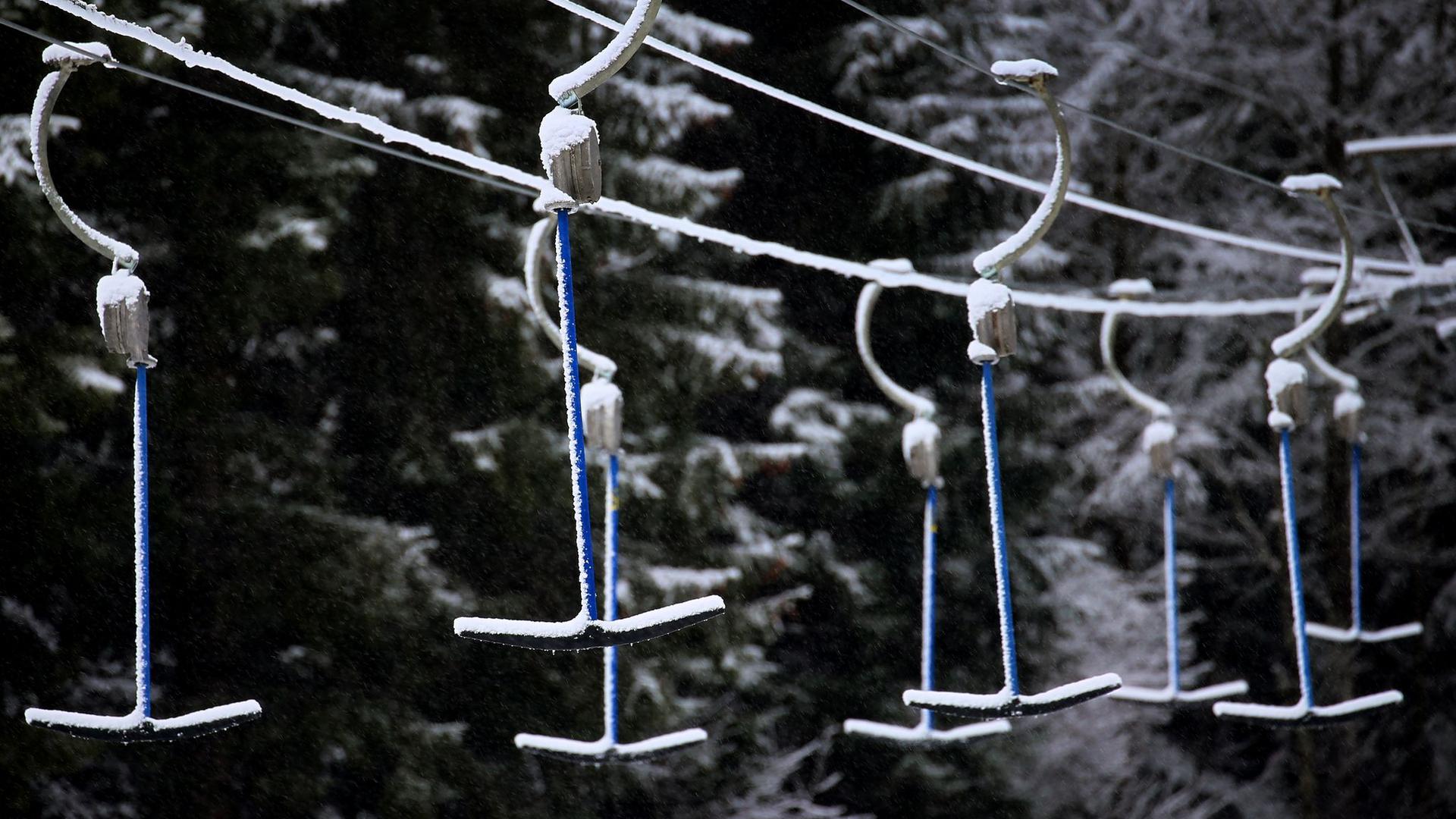 Bügel eines Schleppliftes hängen in schneebedeckter Landschaft. Wegen der Maßnahmen um das Coronavirus müssen Skilifte geschlossen bleiben.