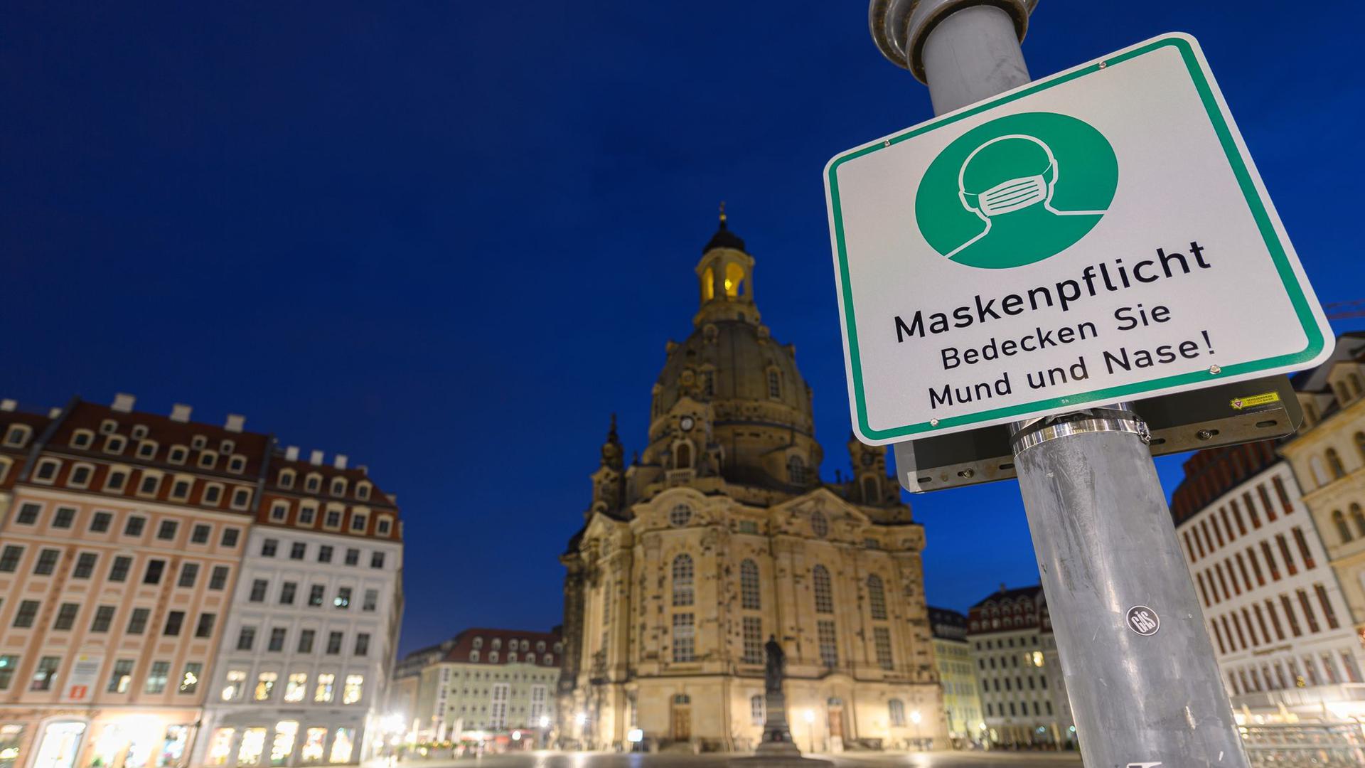 Ein Hinweisschild auf die Maskenpflicht hängt auf dem Neumarkt vor der Frauenkirche an einem Lampenmast.