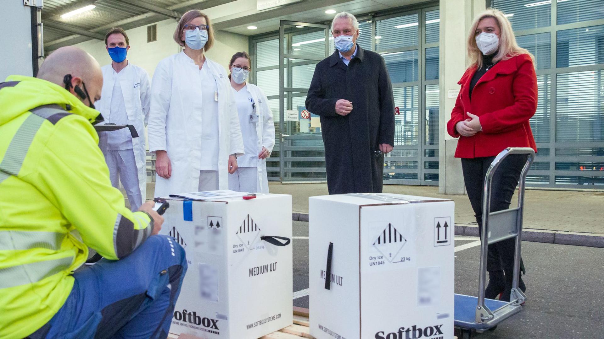Joachim Herrmann (M, CSU), Innenminister von Bayern, und Melanie Huml (r, CSU), Gesundheitsministerin von Bayern, stehen neben Kartons mit den ersten Dosen Corona-Impfstoff für Bayern.