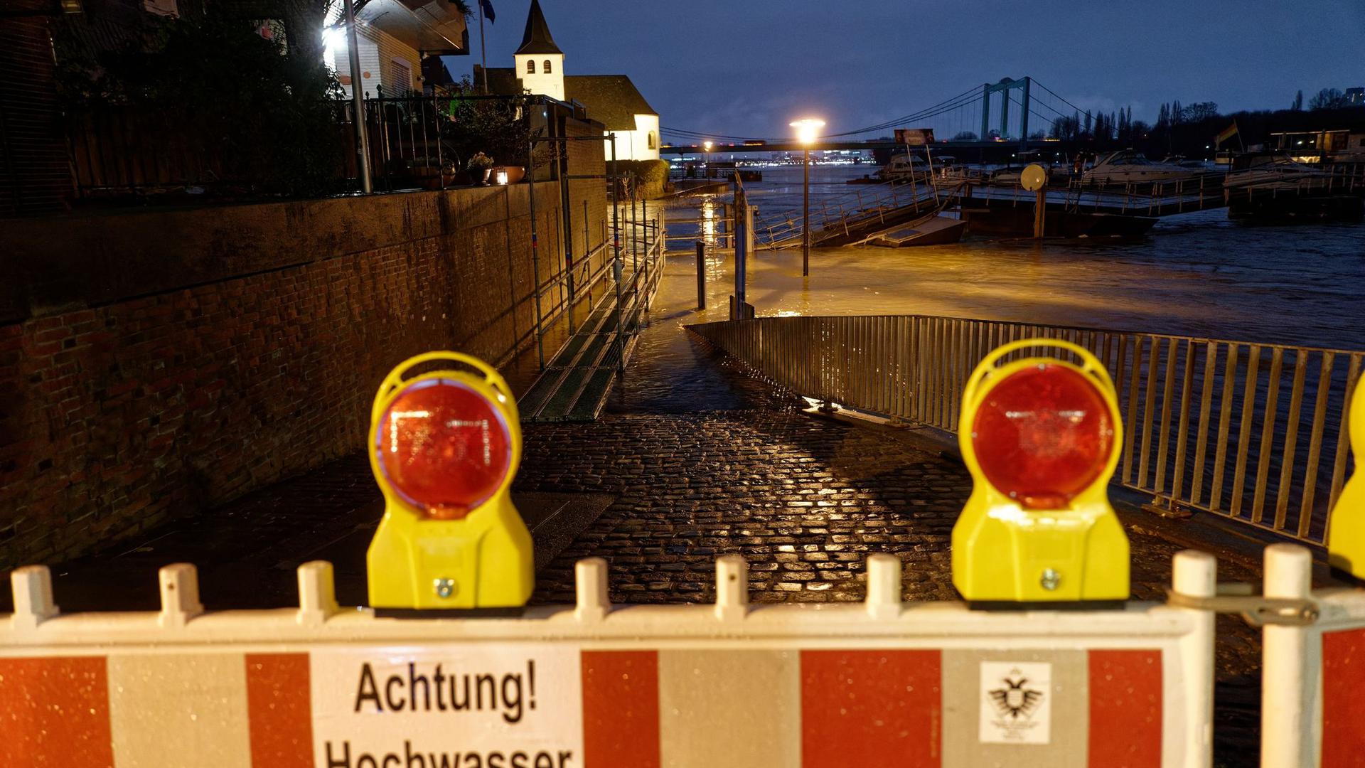 Ein Schild an einer Absperrung warnt vor Hochwasser, nachdem das Wasser des Rheins die Uferstraße in Rodenkirchen überflutet hat.