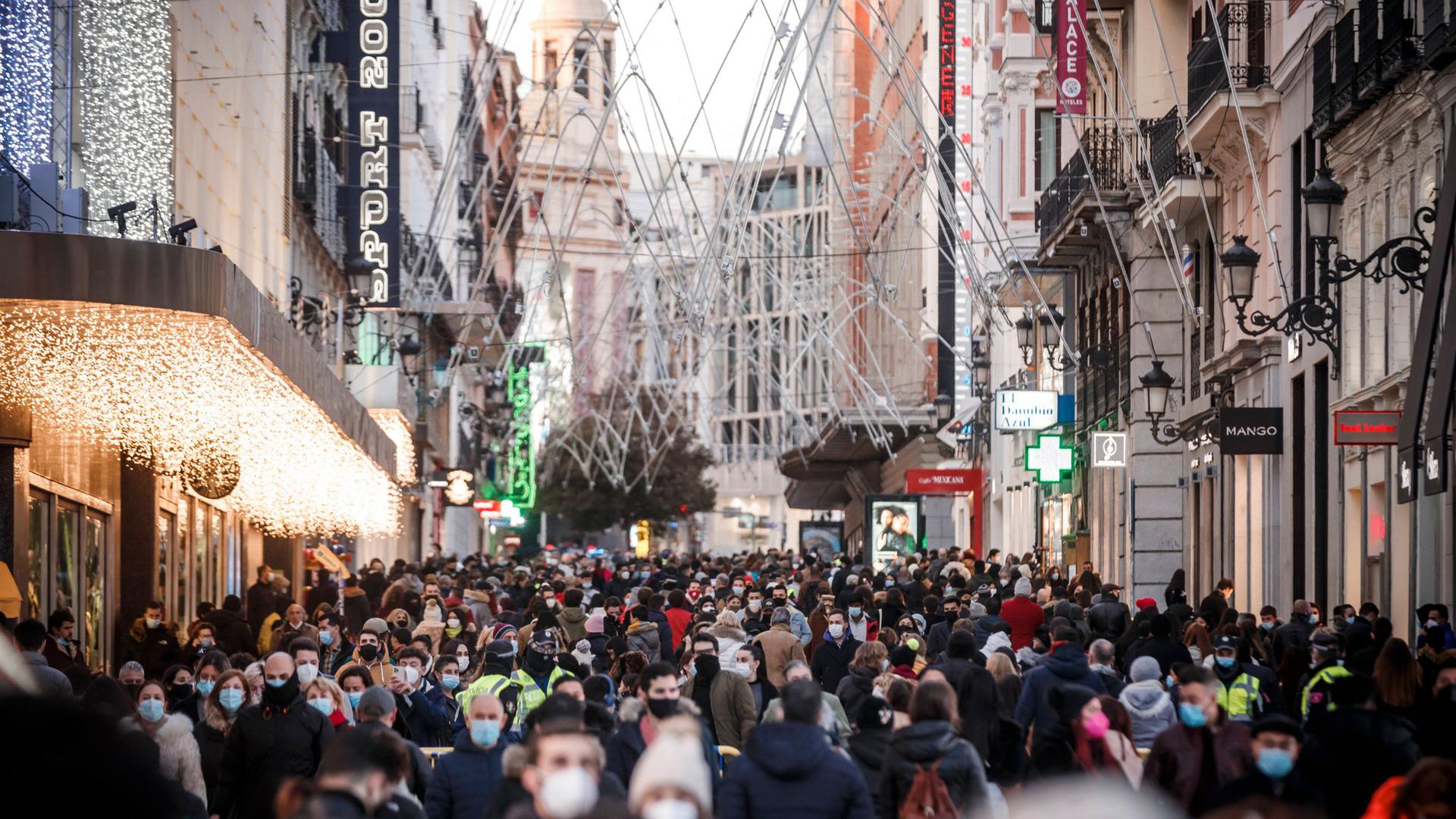 Zahlreiche Menschen mit Mund-Nasen-Schutz gehen eine Einkaufsstraße entlang.
