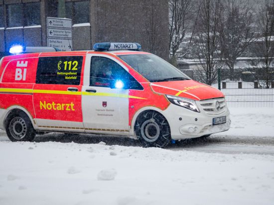 Ein Notarztwagen vom Rettungsdienst fährt mit Blaulicht auf einer zugeschneiten Straße in Bielefeld.
