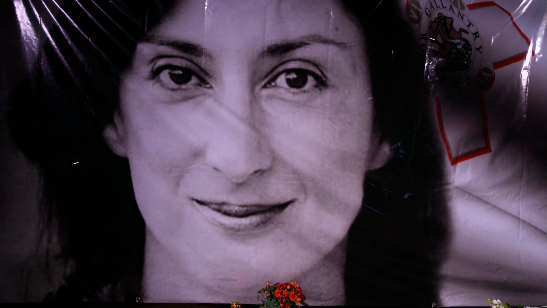 Blumen und eine Kerze liegen vor einem Porträt der ermordeten Enthüllungsjournalistin Daphne Caruana Galizia in Valletta.