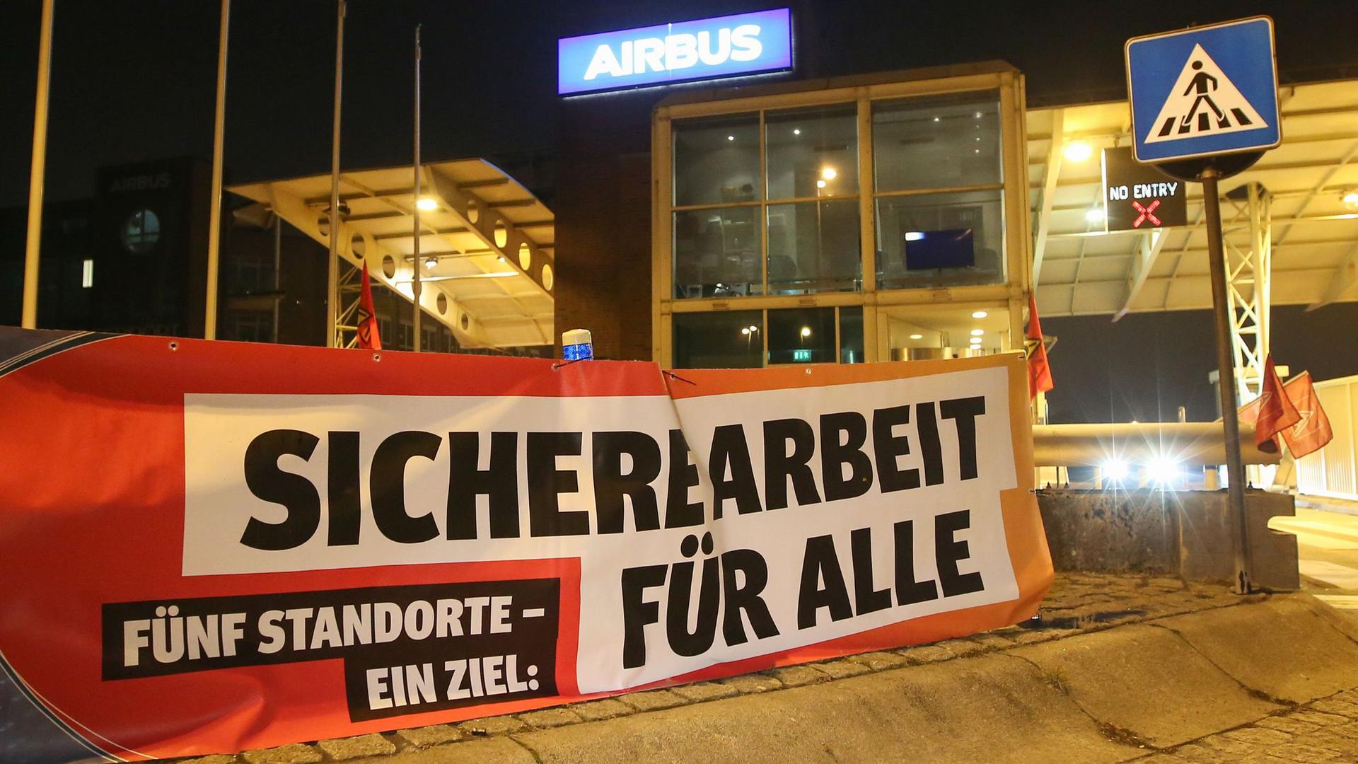 Ein Transparent mit der Aufschrift „Sichere Arbeit für Alle“ hängt vor den Werkstoren des Flugzeugherstellers Airbus in Hamburg-Finkenwerder.