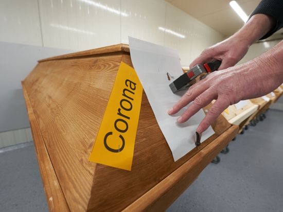 Ein Mitarbeiter des Krematoriums in Dachsenhausen (Rheinland-Pfalz) bringt an einem Sarg die Markierung „Corona“ an.